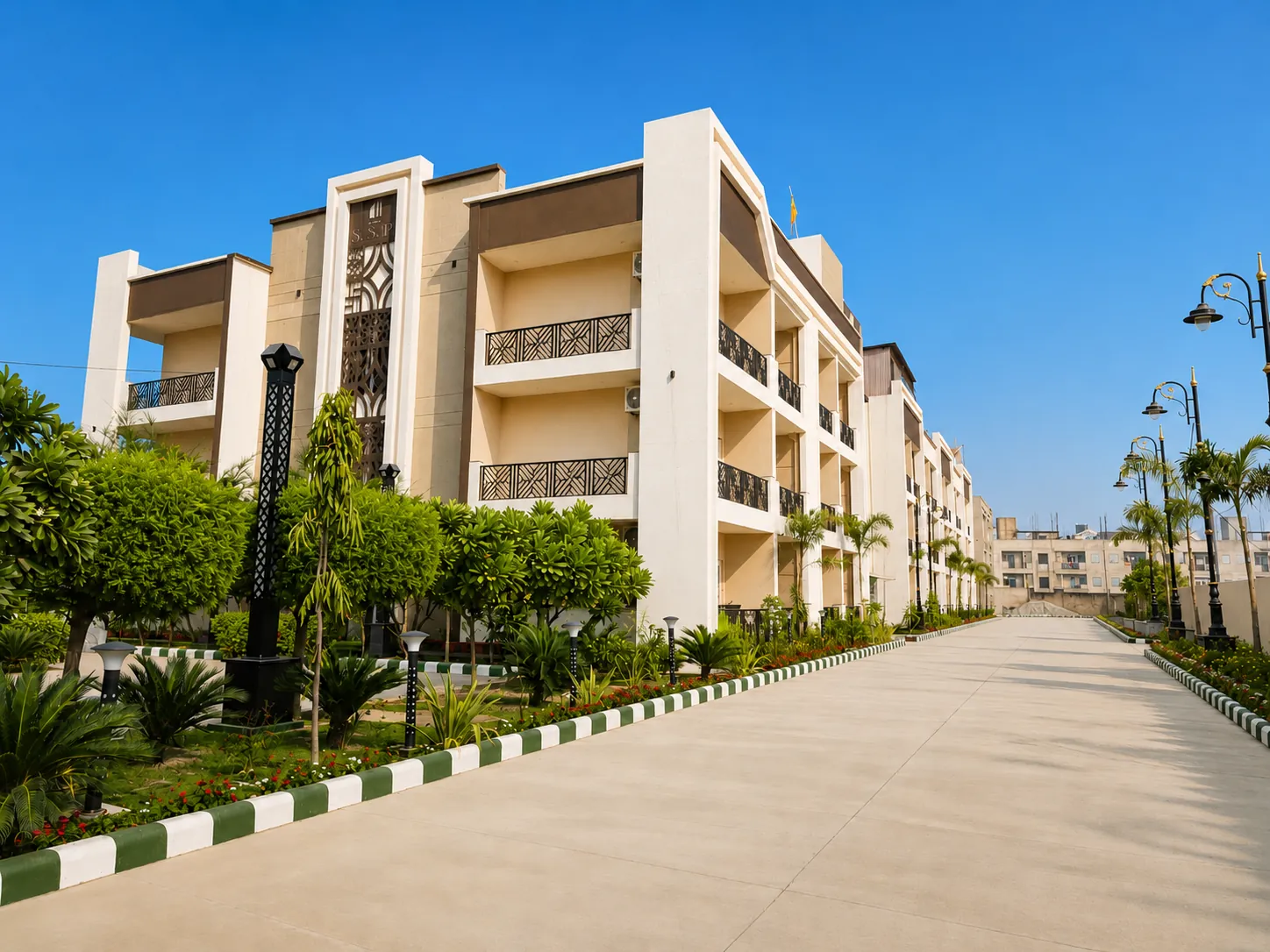 Shri Sadhna Dham, a low-rise residential building with a cream façade and carved screen panels, beside a landscaped drive